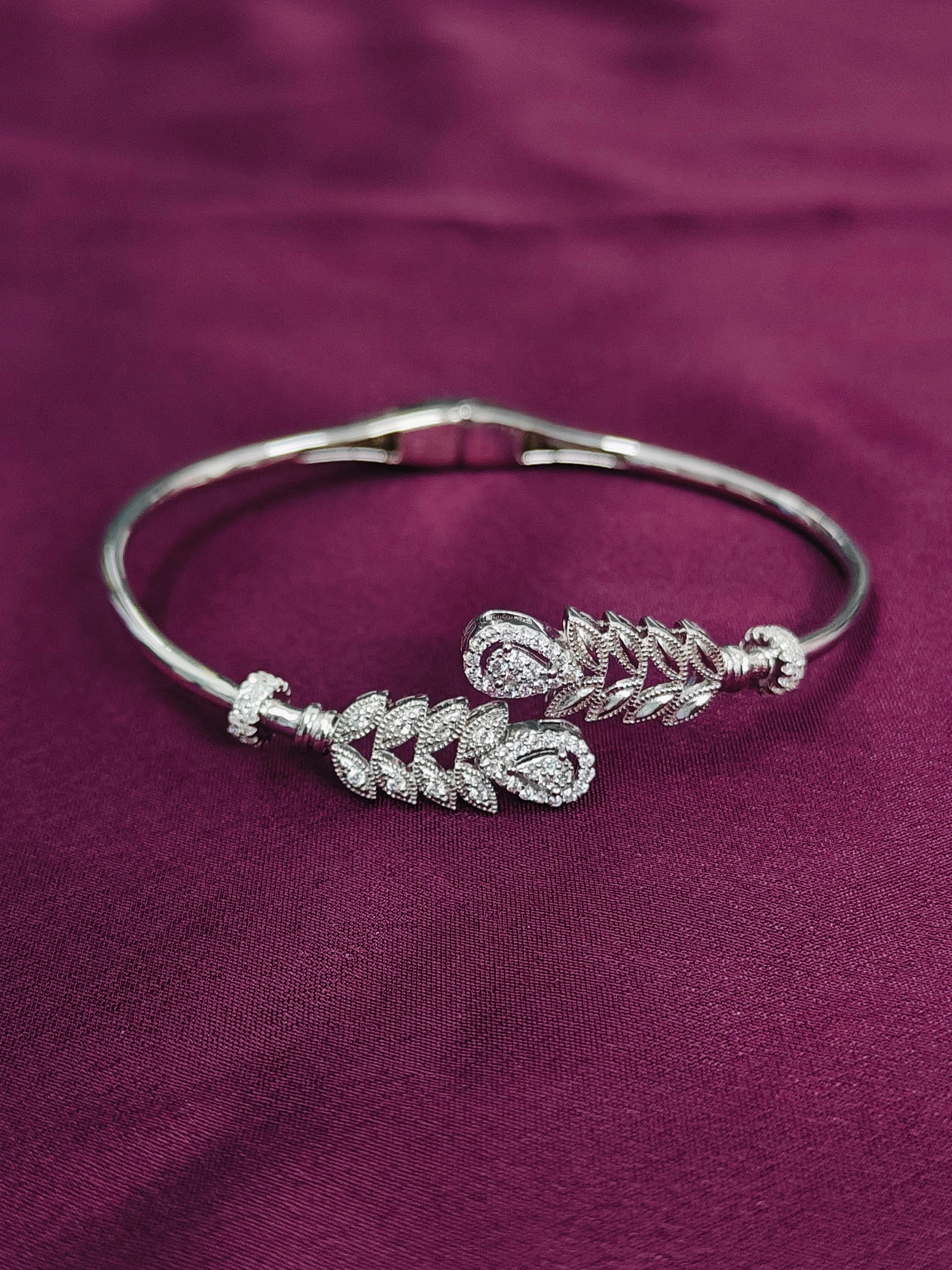 Silver bracelet with leaf designs on a purple fabric background